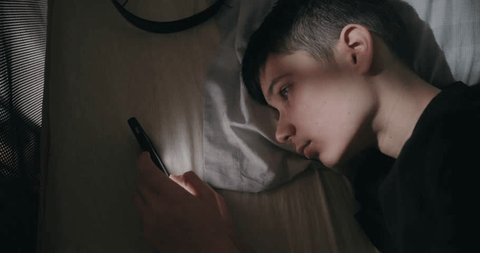 Teen boy scrolling phone late at night
